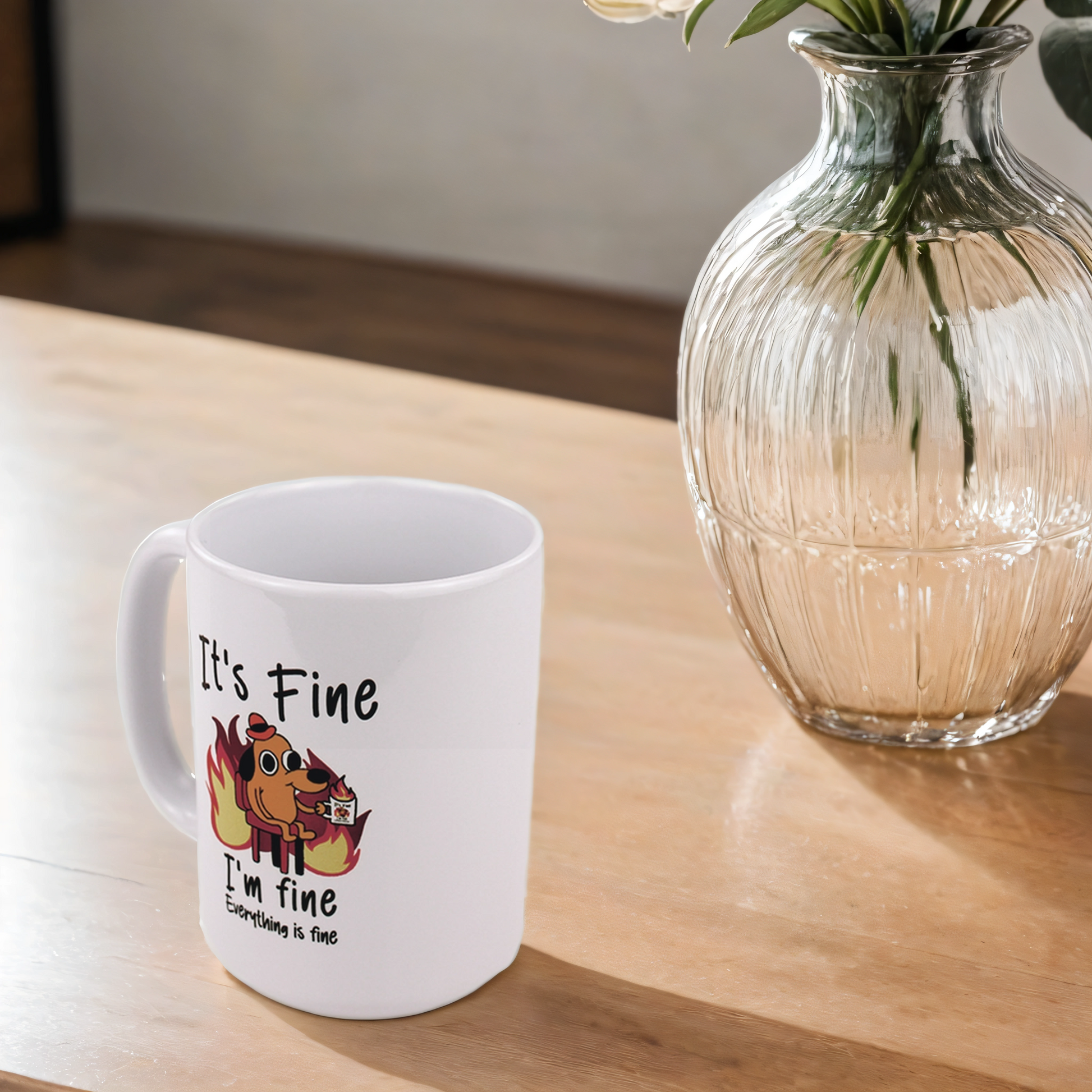 White mug with a cartoon design and text on a wooden table next to a glass vase with plants.