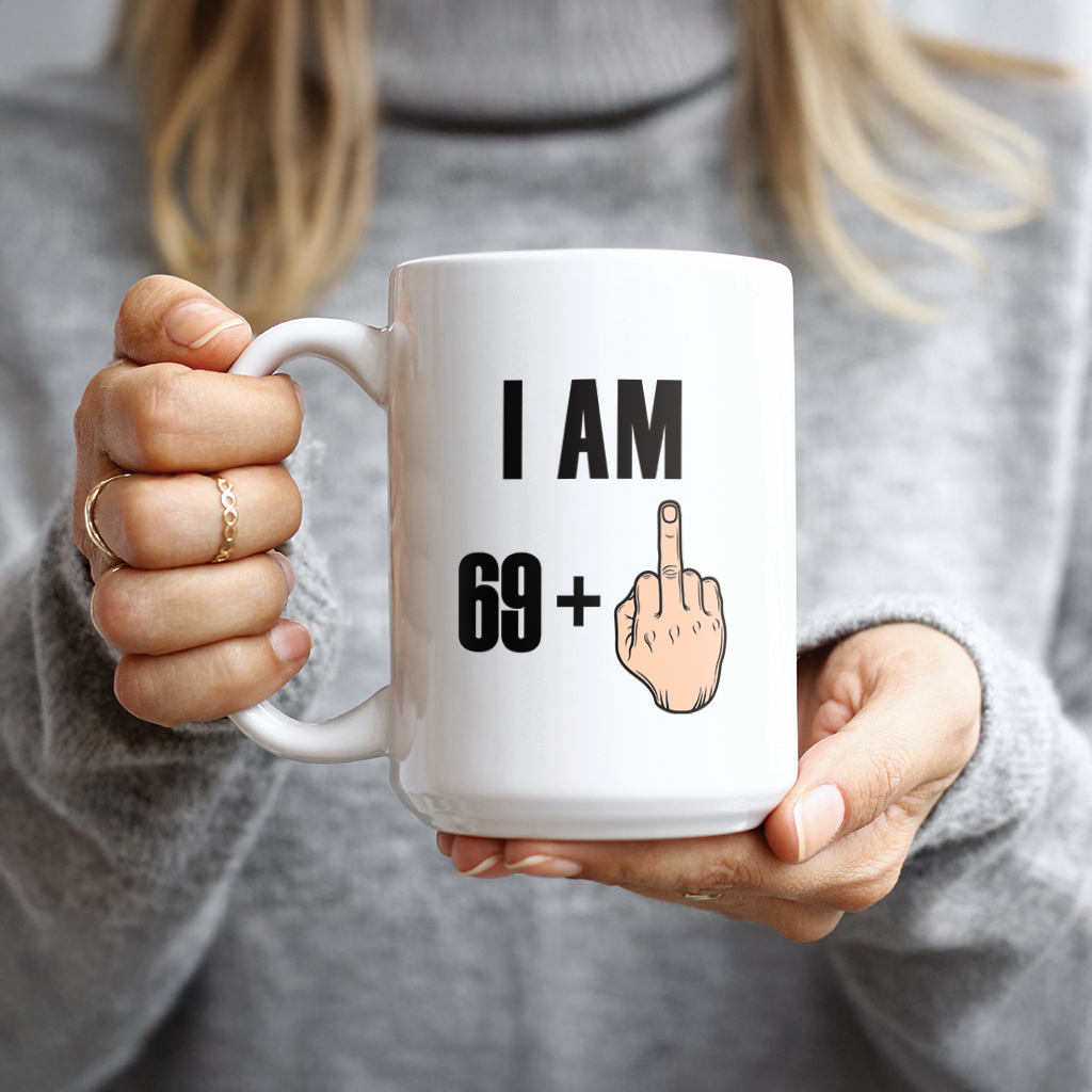 Hand holding white mug with I Am 69 Plus One design