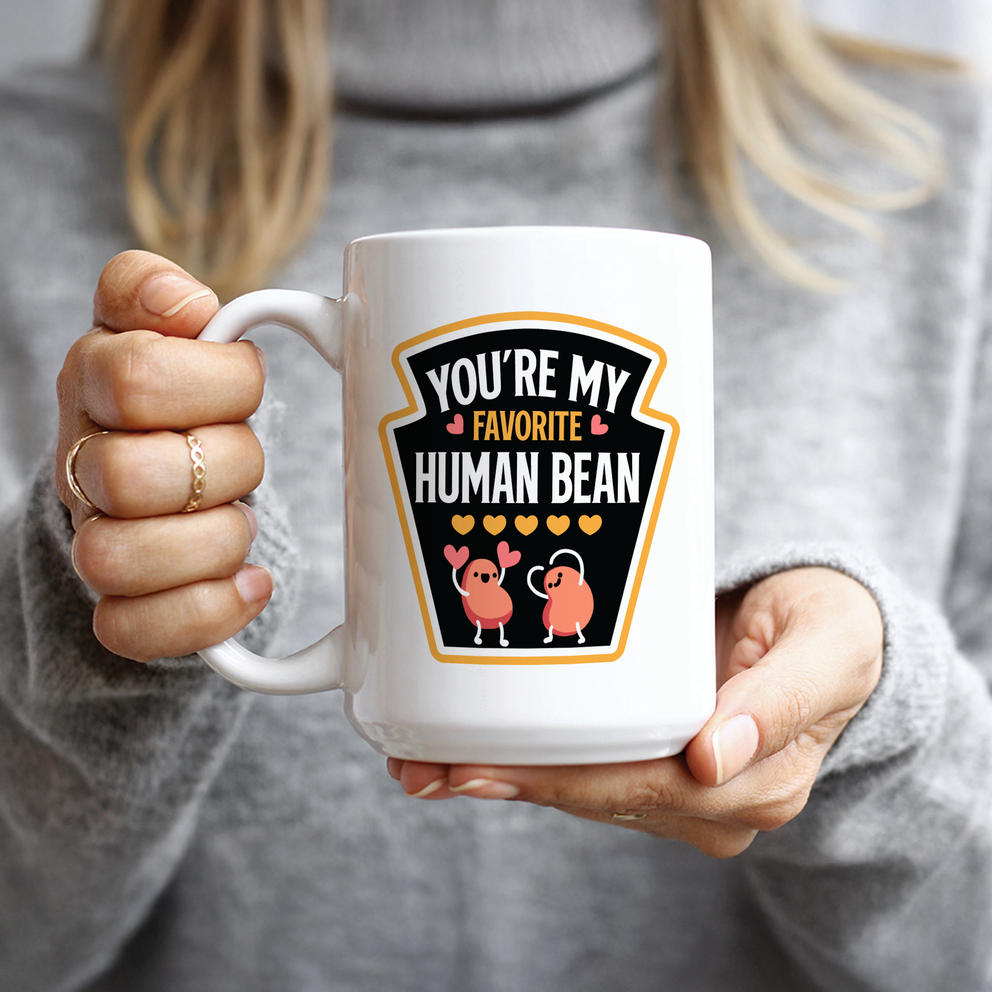 Hand holding white mug with cartoon beans making heart gestures